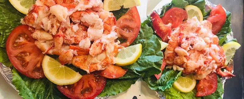 Two lobster rolls plated on lettuce with tomato and lemon at Red's Eats