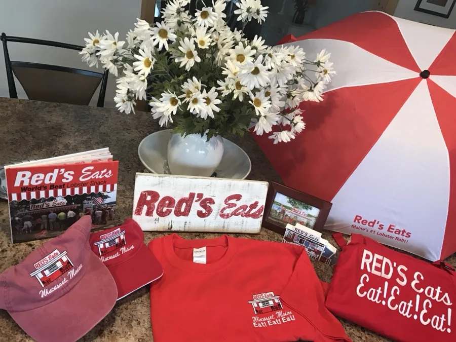 Red's Eats merchandise flat-lay including the Red's Eats book, hats, t-shirts and a red-and-white umbrella